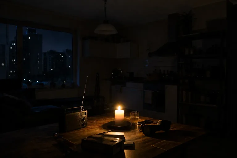Dunkle Küche während eines Stromausfalls, nur eine Kerze, Kurbelradio und Taschenlampe auf dem Tisch